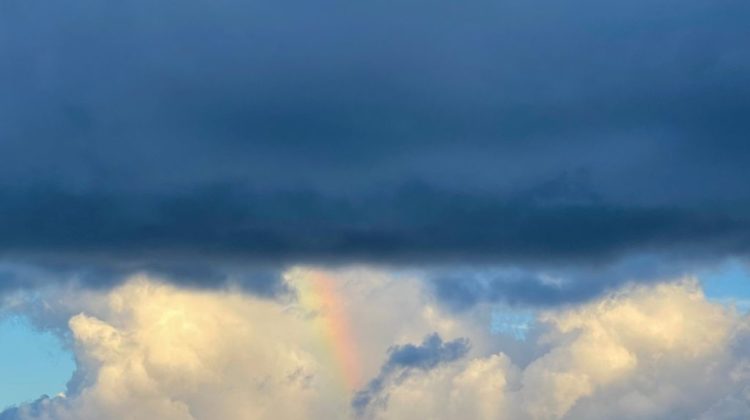 dark storm cloud over white clouds with small piece of a rainbow