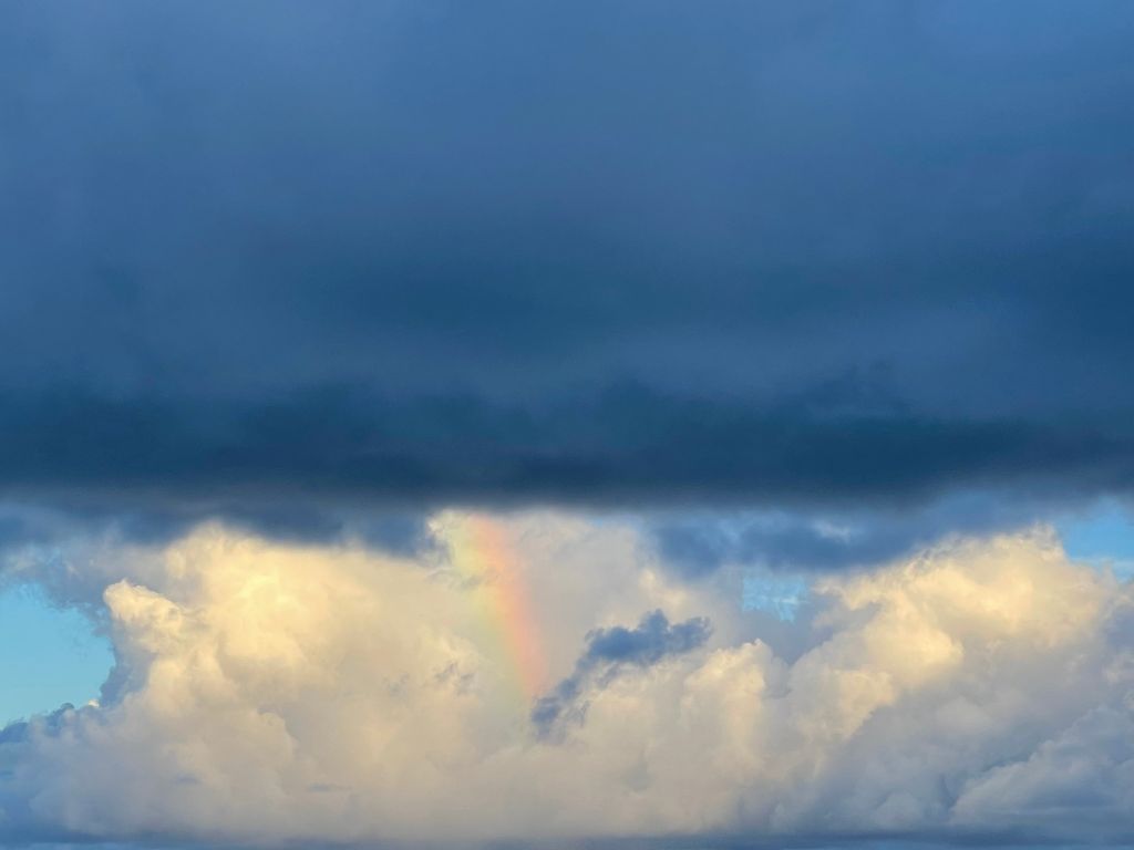 dark storm cloud over white clouds with small piece of a rainbow