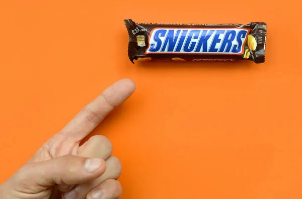 finger points to a Snickers candy bar