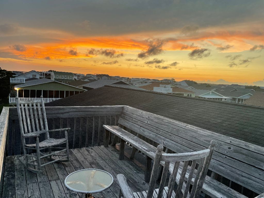 Rocking chairs on a roof top with a sunset in the sky