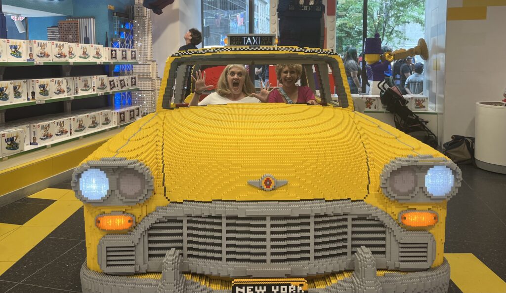 Two women in giant yellow taxi made out of Legos