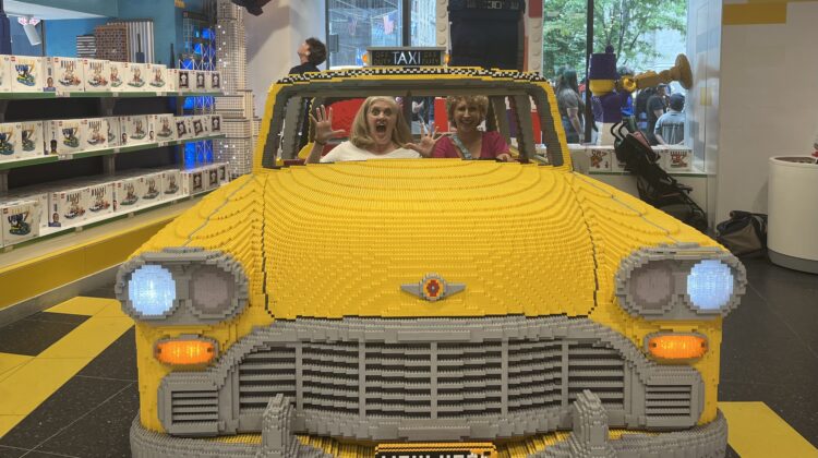 Two women in giant yellow taxi made out of Legos