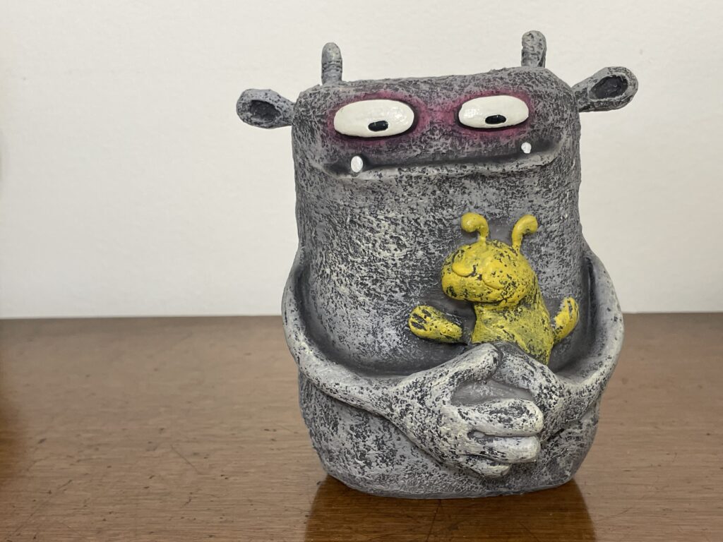 gray monster figure holding a yellow bunny rabbit stuffed animal