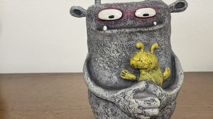 gray monster figure holding a yellow bunny rabbit stuffed animal